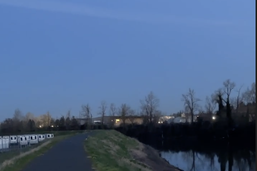 a paved path in late evening above a steep bank to the right that slopes down to a wide creek